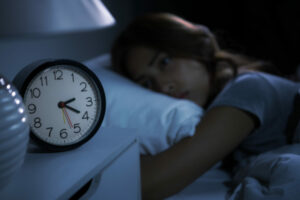 Girl in bed next to clock experiencing Insomnia